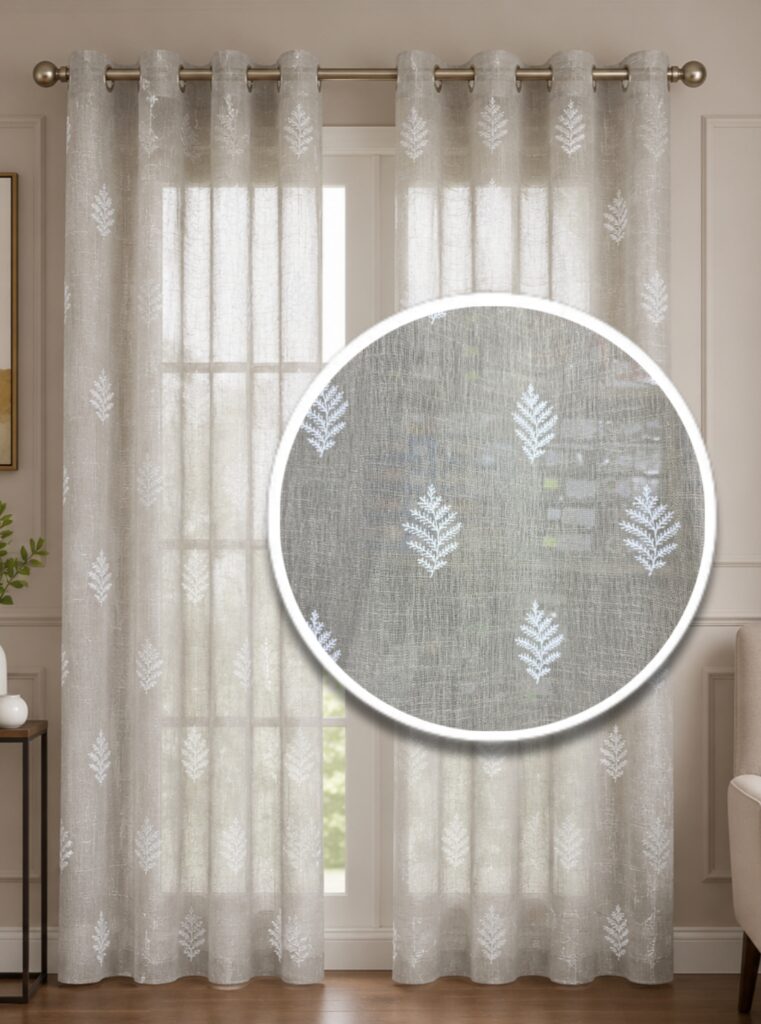 Neutral oatmeal-colored faux linen sheer curtain panel featuring white embroidered leaf patterns hung on a brass grommet rod in front of a bright window.