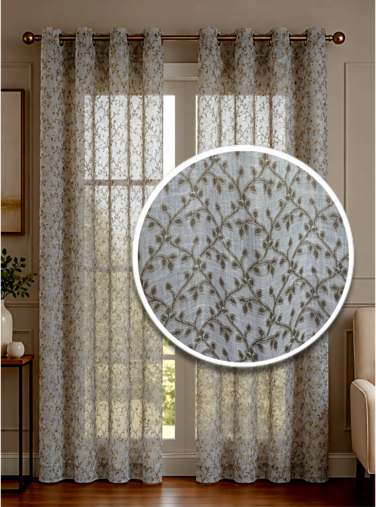 Elegant cream sheer curtains with a brown leaf and vine embroidery pattern hanging from a bronze grommet rod in a brightly lit living room