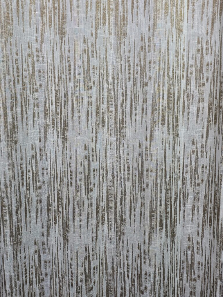 Modern off-white sheer curtains with a grey and taupe distressed vertical stripe pattern hanging from a bronze grommet rod